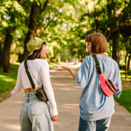 Multiracial two women talking and gesturing while walking together in green park